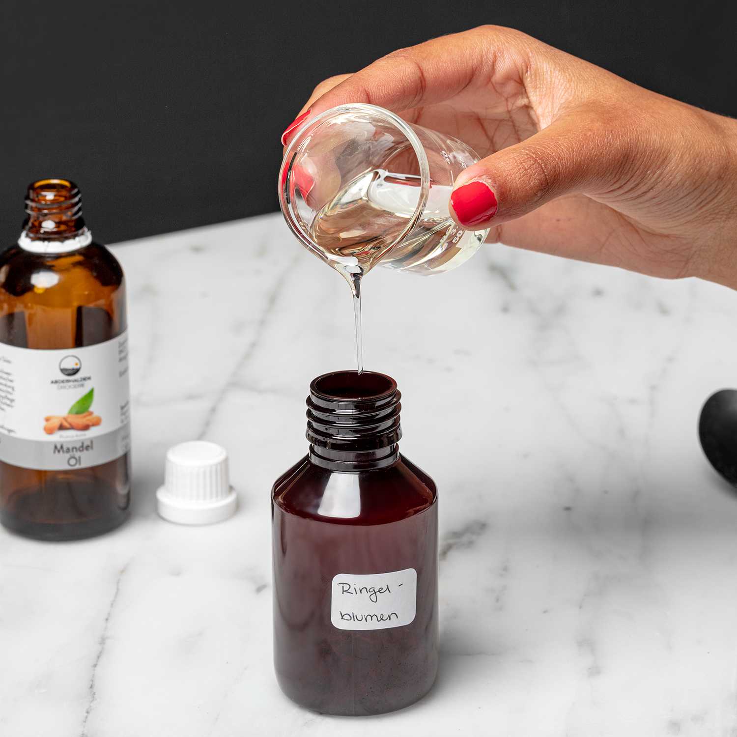 Hand füllt Öl aus kleinem, gläsernen Messbecher in mit "Ringelblumen" beschriftete Braunglasflasche