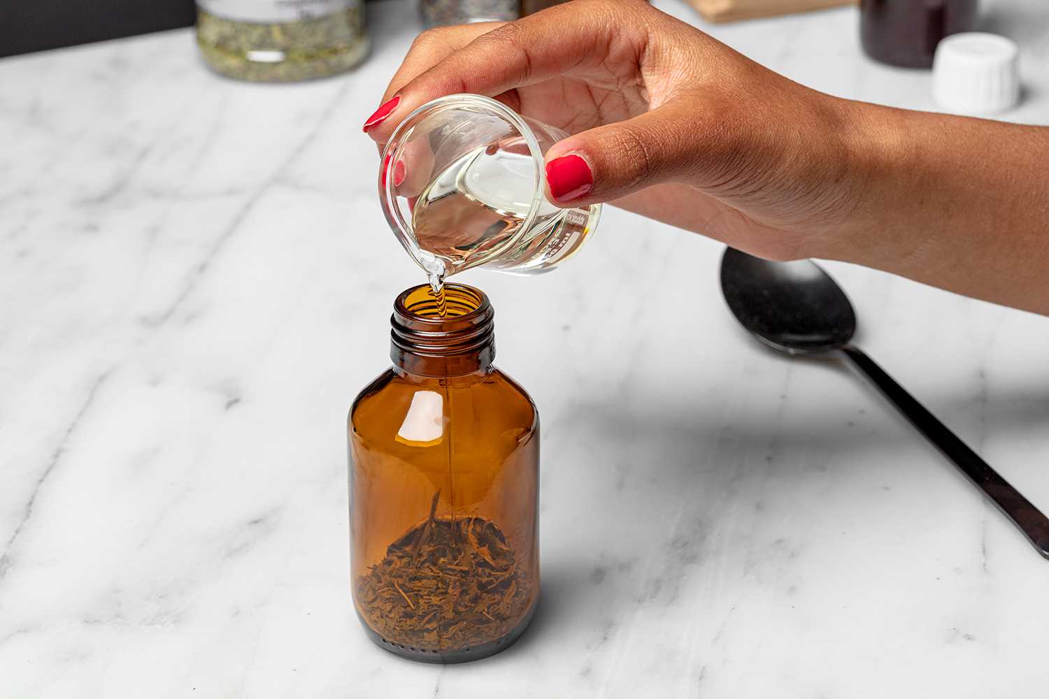 Hand gibt abgemessenes Öl in Braunglasflasche mit Lavendelblüten