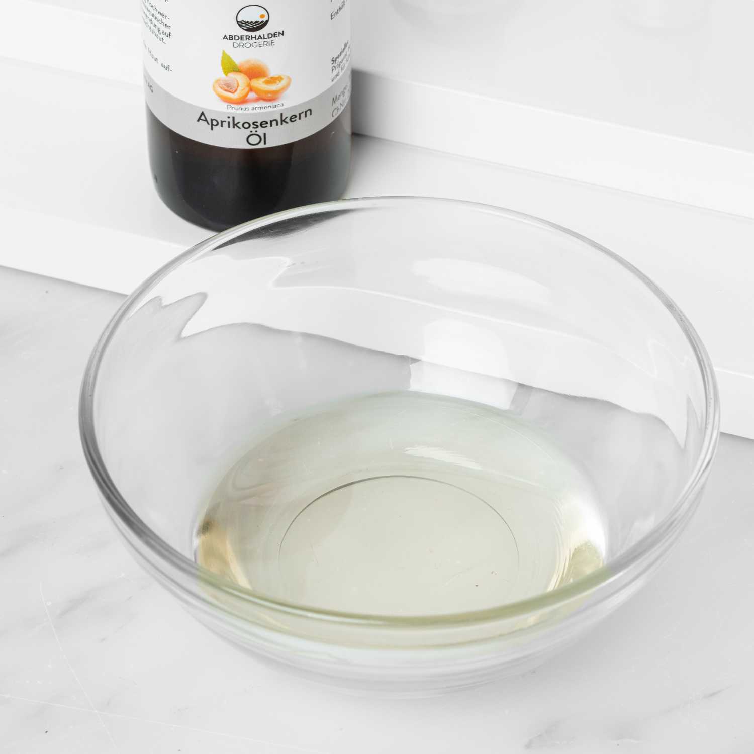 Aprikosenkernöl abgewogen in kleiner Schale mit Flasche im Hintergrund