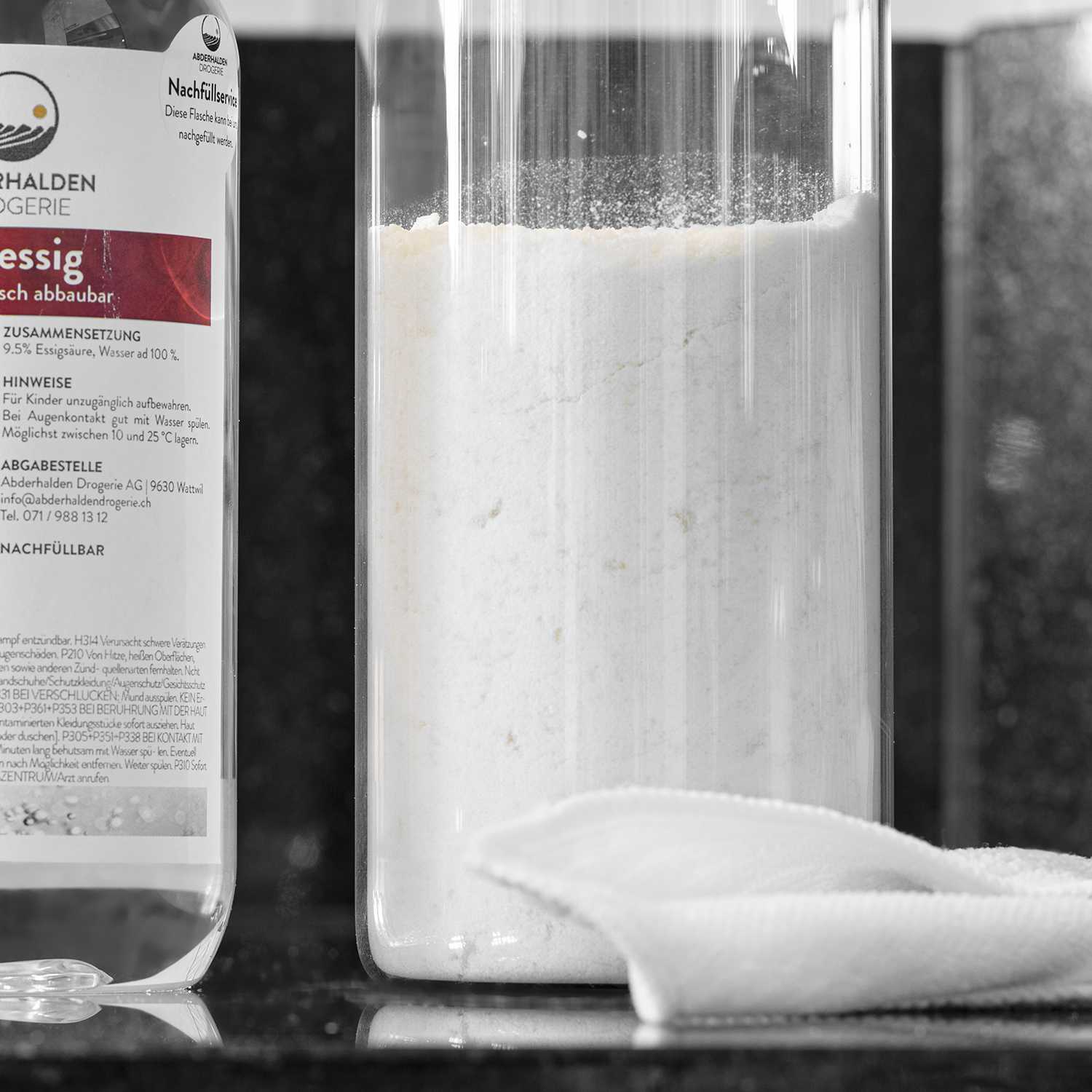 Fertiges Pulver-Weiss-Waschmittel in Glasgefäss, dahinter Putzessig-Flasche