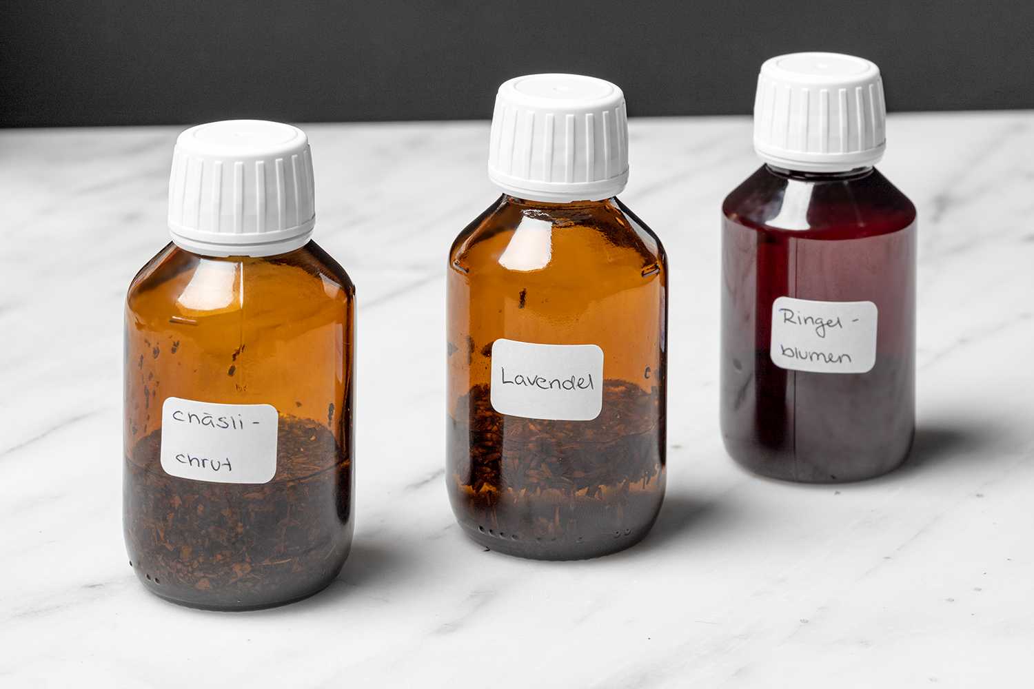 Drei kleine braune Flaschen mit weissem Verschluss, angeschrieben mit "Chäslichrut", "Lavendel" und "Ringelblume", darin befinden sich die entsprechenden Pflanzen mit Öl